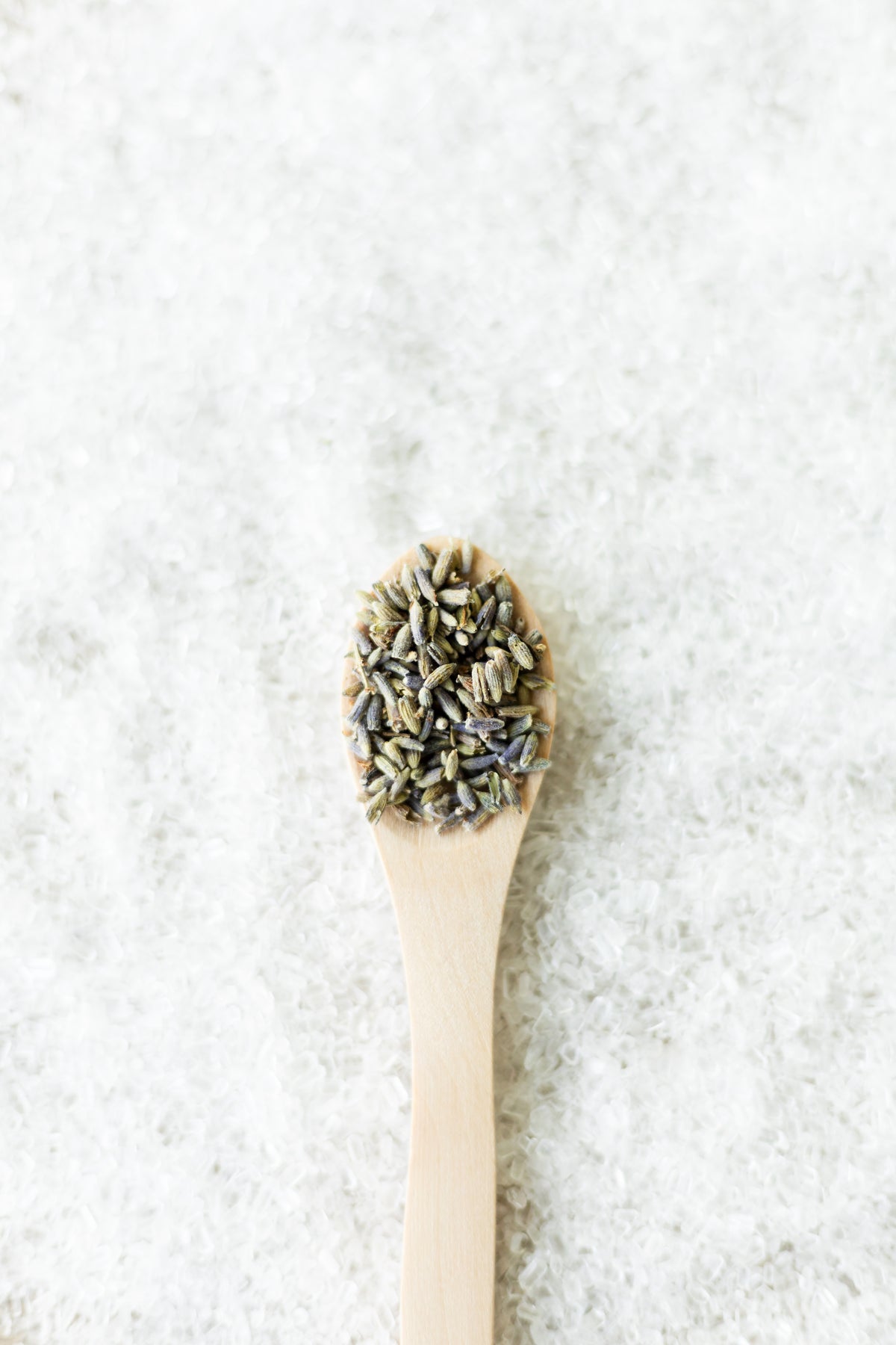 Cuchara de madera con botones de lavanda seca sobre cama de sal gruesa blanca, composición vertical minimalista