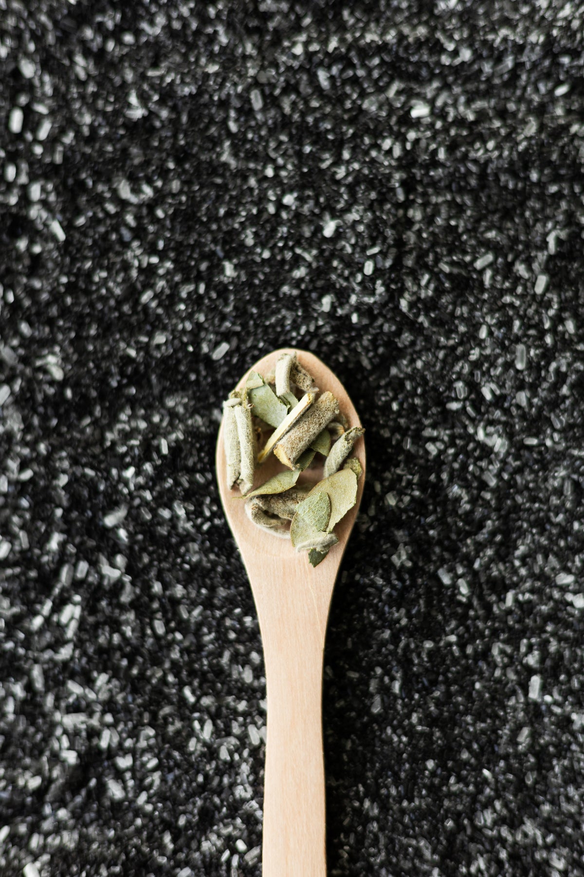 Cuchara de madera con hojas verdes de salvia sobre cama de sal gruesa negra, composición vertical minimalista